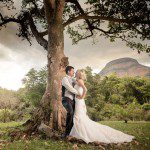 Newlyweds under a large Lowveld tree with the Drakensberg mountains behind, a stunning mountain-view wedding venue in Limpopo.