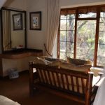 A beautifully furnished safari-style bedroom at Moholoholo Forest Camp, featuring twin beds, soft lighting, and mosquito net drapes.