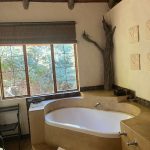 Spacious bathroom at Moholoholo Forest Camp with a large bathtub, natural light, and a forest-view window for a serene ambiance.