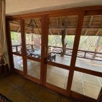 Wooden-framed glass doors at Moholoholo Forest Camp open onto a scenic outdoor patio, blending indoor and outdoor spaces beautifully.